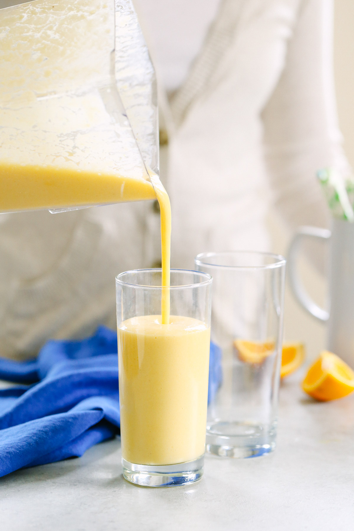 Mango and turmeric smoothie being poured into a tall drinking glass from a blender jar.