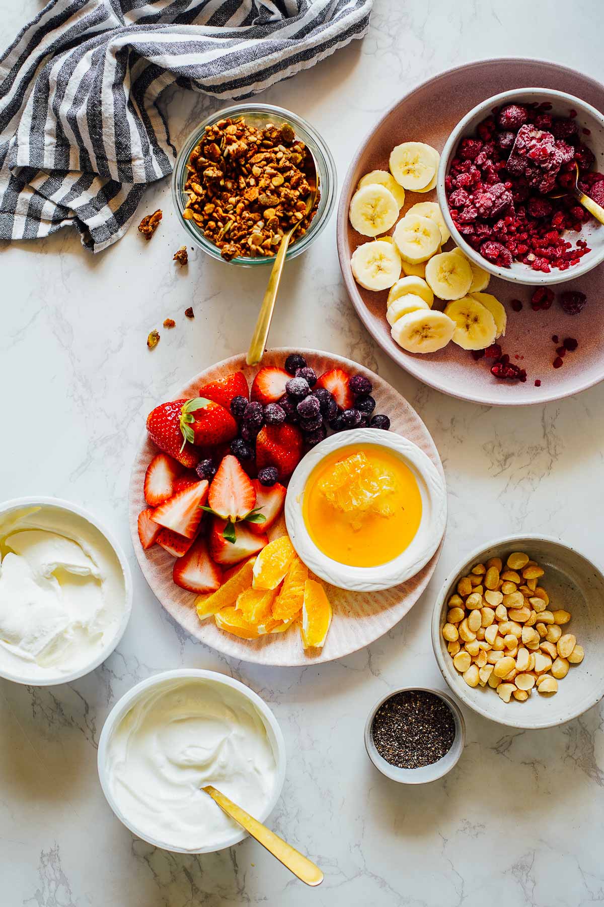 Healthy yogurt bowls: yogurt, fruit, honey, and granola spread out on a countertop.
