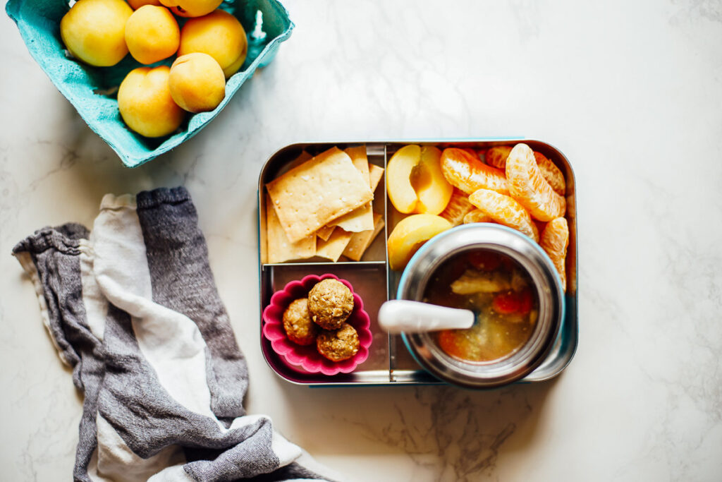 Lunchbox with thermos: chicken noodle soup inside the thermos with oranges and energy bites on the side.