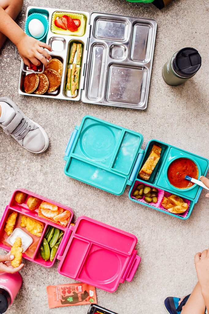 3 lunchboxes on the ground: with chicken nuggets, with soup, and with pancakes.