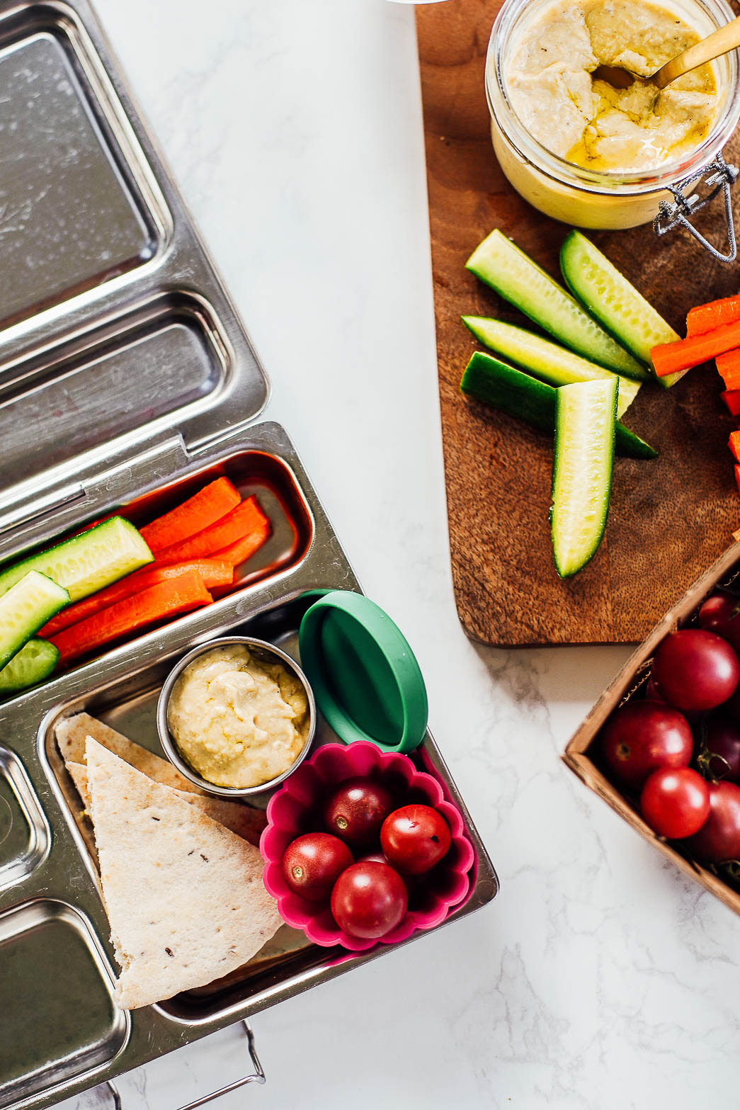 Vegetarian lunchable: hummus, pita bread, cherry tomatoes, cucumber sticks, carrot sticks in a bento box.
