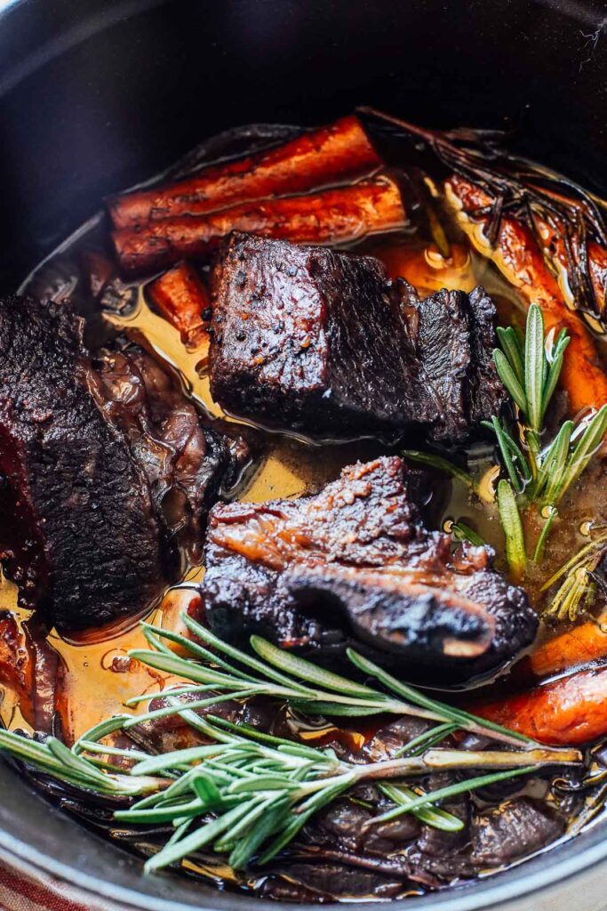 Short ribs in a dutch oven with carrots and rosemary.
