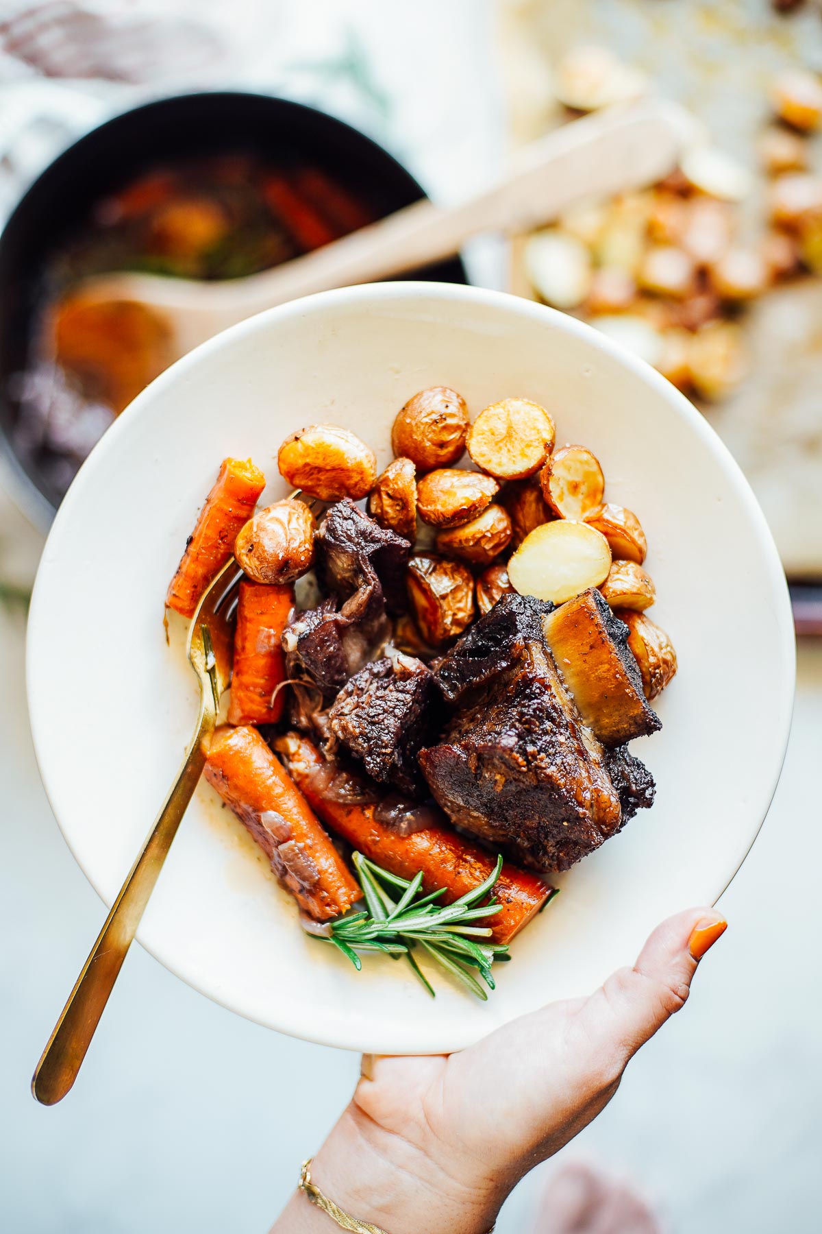 Short ribs in a bowl with potatoes and carrots.