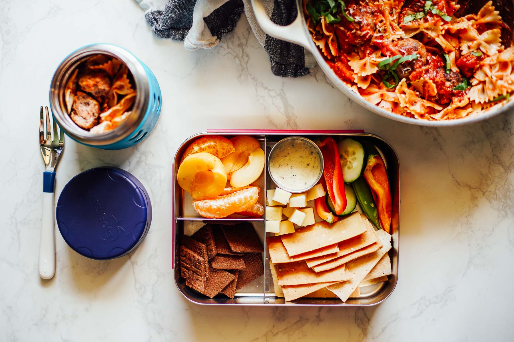 Leftover spagetti in a thermos with crackers, vegetables, apricots, and chocolate cookies in a bento box.