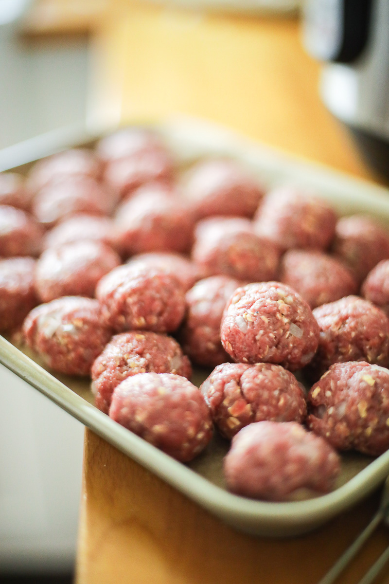 24 meatballs formed into tight balls sitting on a sheet pan.