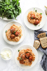 Meatballs and spaghetti sauce mixed with spaghetti noodles on three white plates.