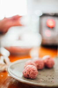 Forming meatballs in hands and a few meatballs on a plate.
