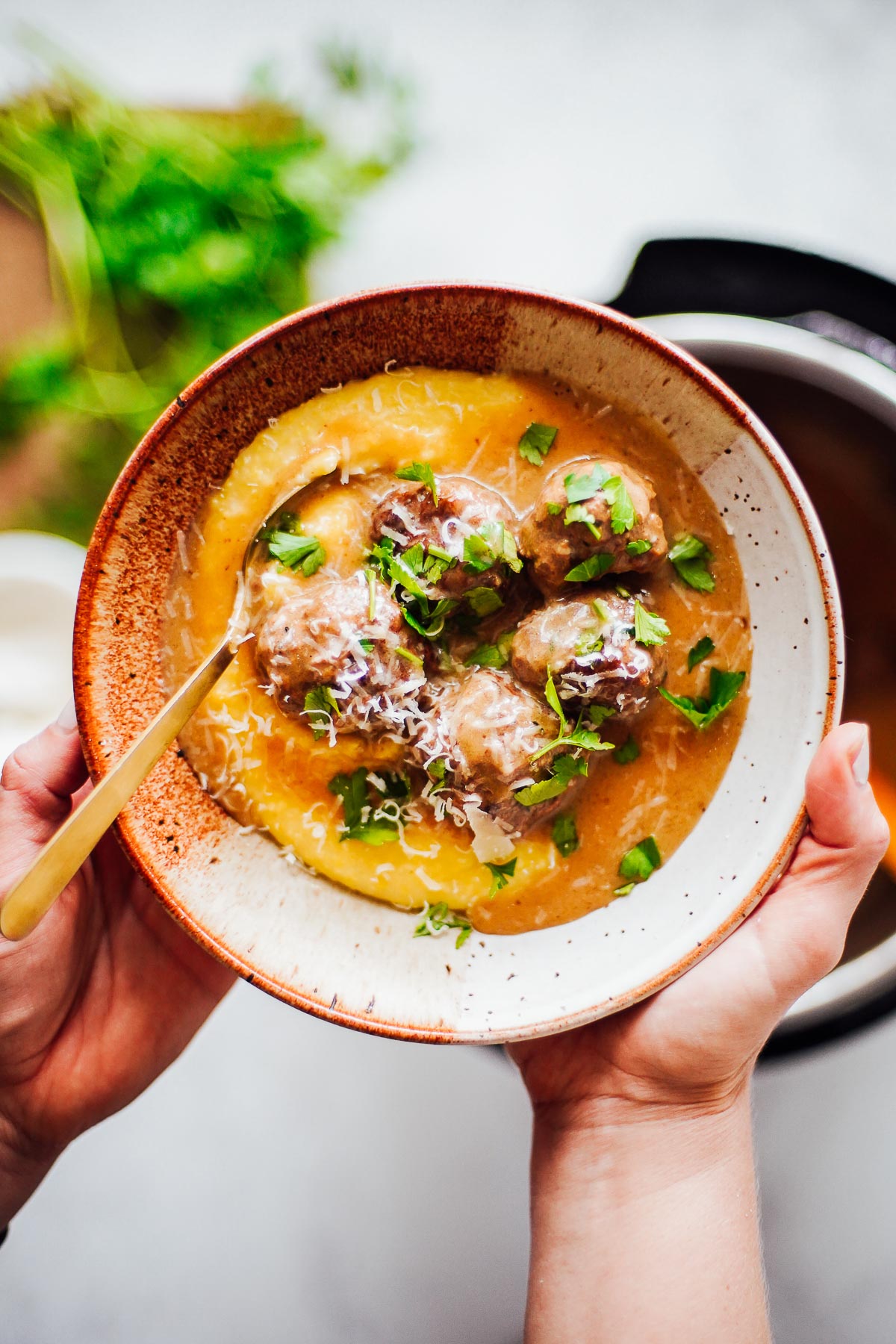 Cooked Swedish meatballs in a gravy sauce served over polenta in a brown ceramic bowl.
