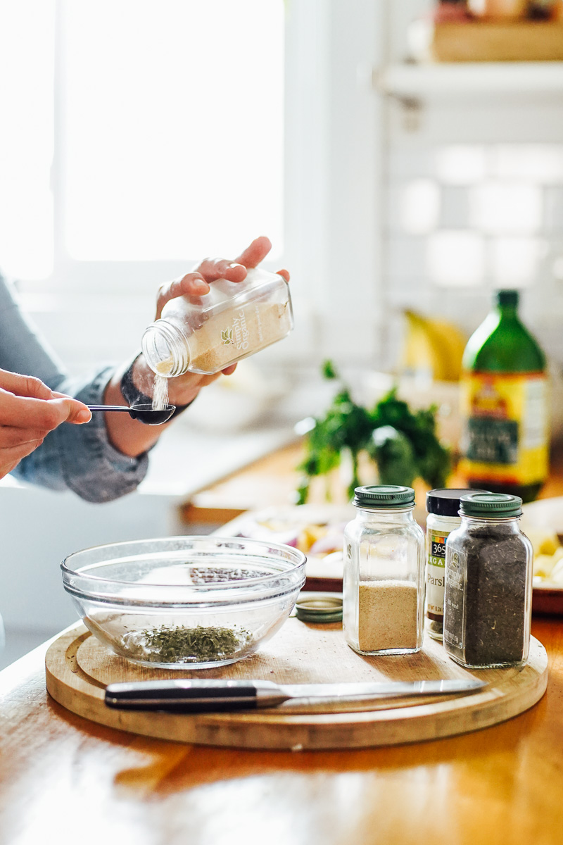 Pouring garlic powder from a glass jar into a measuring spoon with spices on the counter in the background.