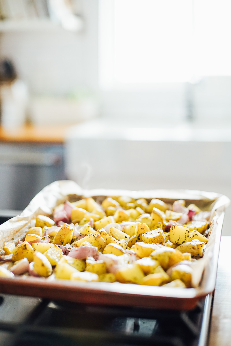 Chopped golden potatoes and red onion wedges on a sheet pan, on top of the oven.