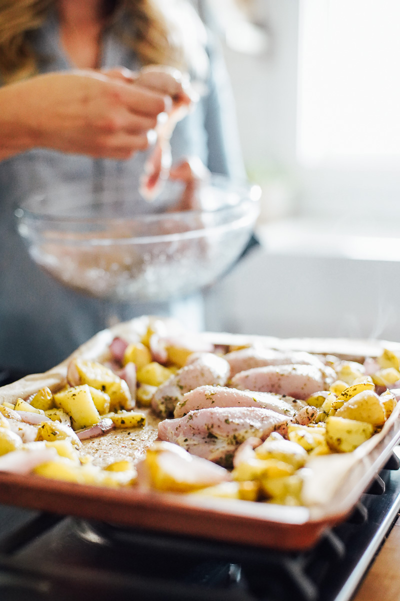 Adding seasoned chicken thighs to the center of the sheet pan with potatoes around the perimeter of the pan.