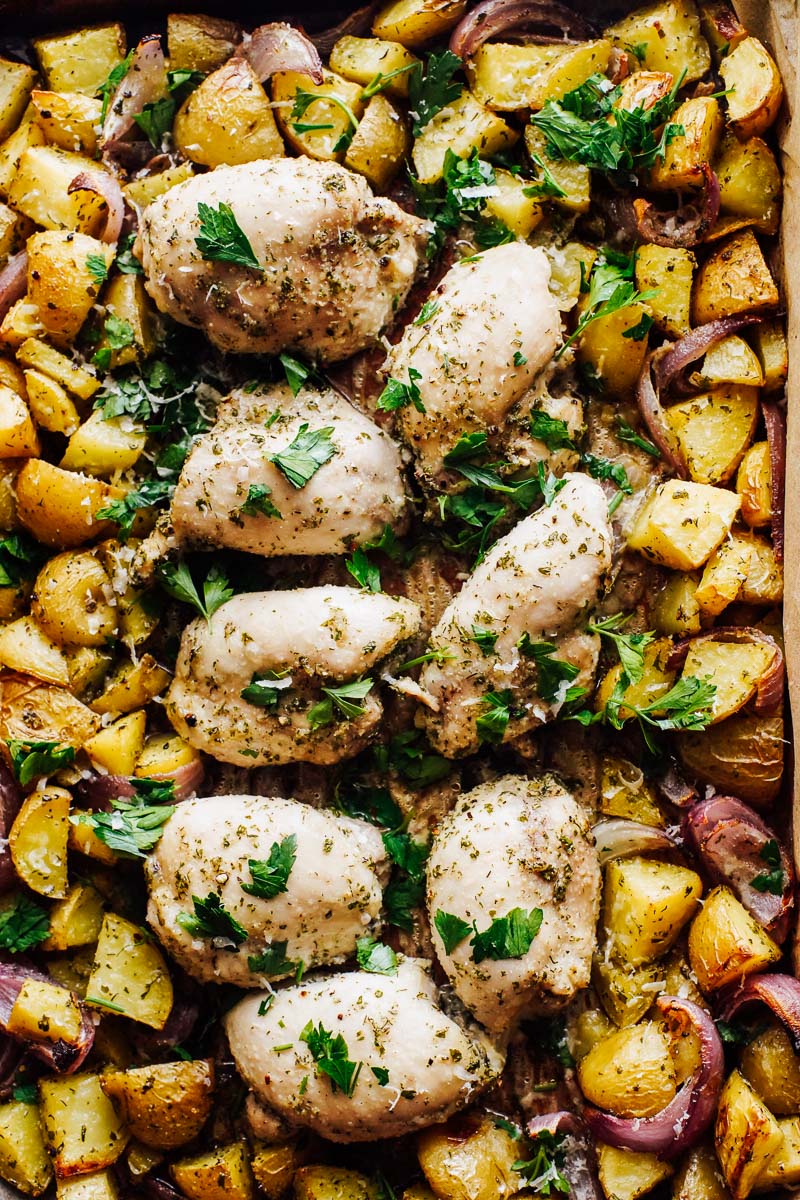 Cooked chicken and potatoes on a sheet pan topped with chopped parsley.