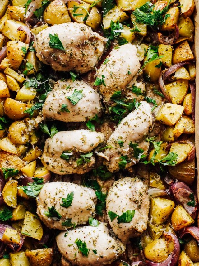 Cooked chicken and potatoes on a sheet pan topped with chopped parsley.