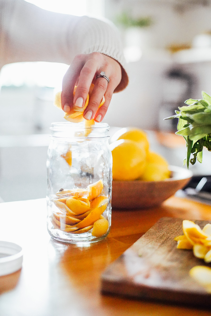 Adding orange and lemon peels to a glass quart-size jar.