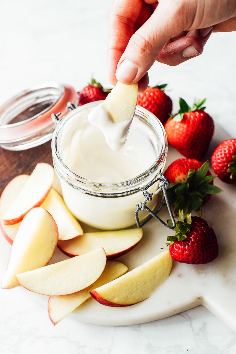 Yogurt dip in a glass jar with apple slices and strawberries.