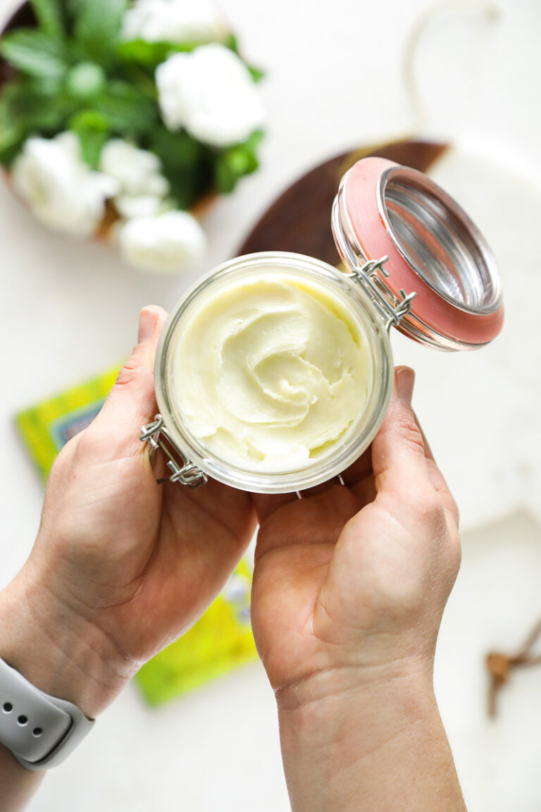 Hands holding a glass jar with white, homemade whipped body body butter inside.