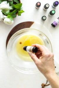 Adding essential oil to the chilled body butter mixture in a glass bowl.