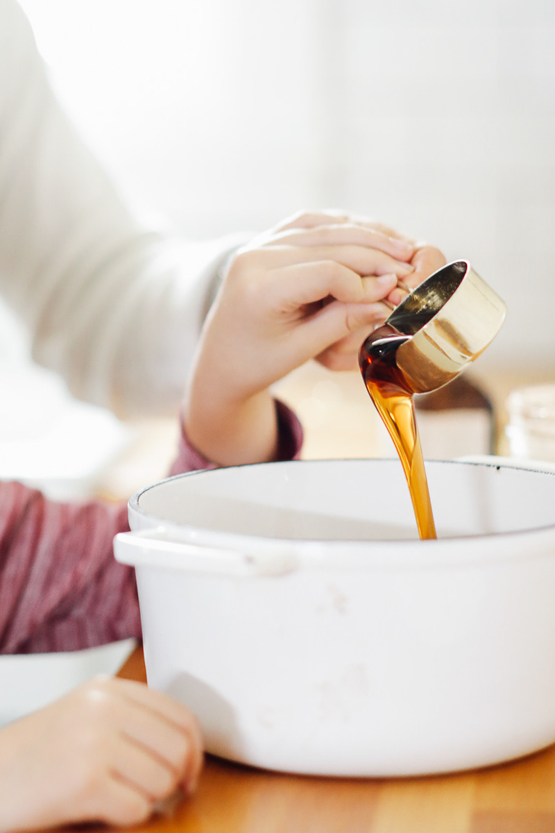 Pouring maple syrup from a measuring cup into a white dutch oven.