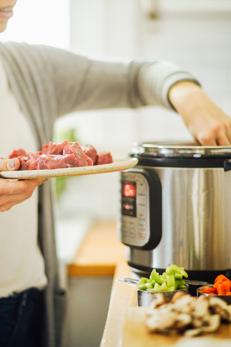 Adding the seasoned beef from a plate into the hot Instant Pot.