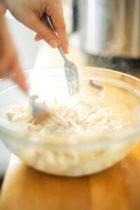 Shredding the chicken in a medium-size bowl.