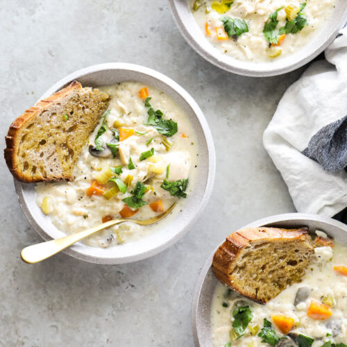 Three bowls of chicken and rice soup with a slice of bread in each soup.