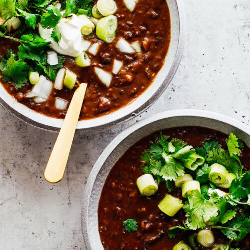 Black bean soup in bowls topped with cilantro, green onions, and sour cream.