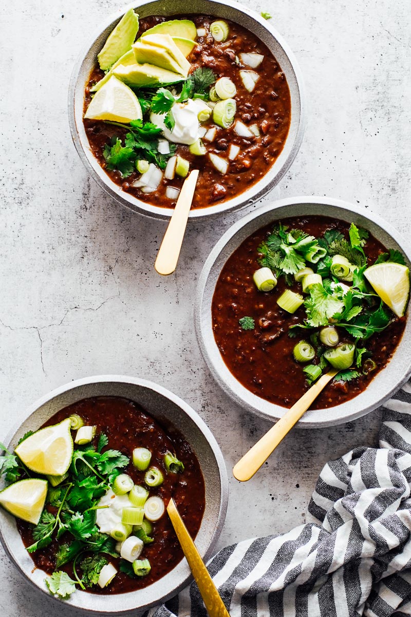 Three black bean soup bowls with toppings: cilantro, sour cream, green onions. 