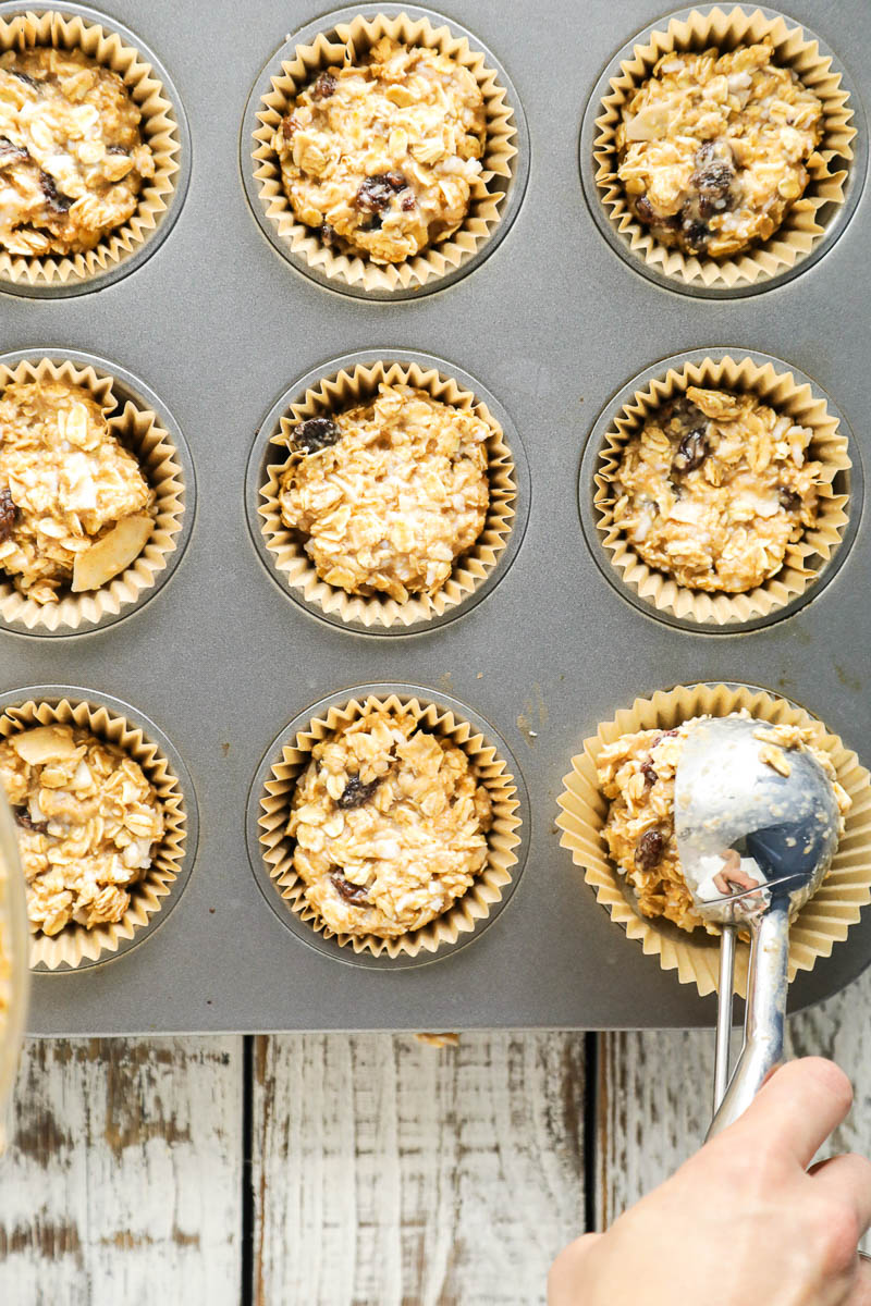 Spooning oatmeal cup batter into a muffin pan.