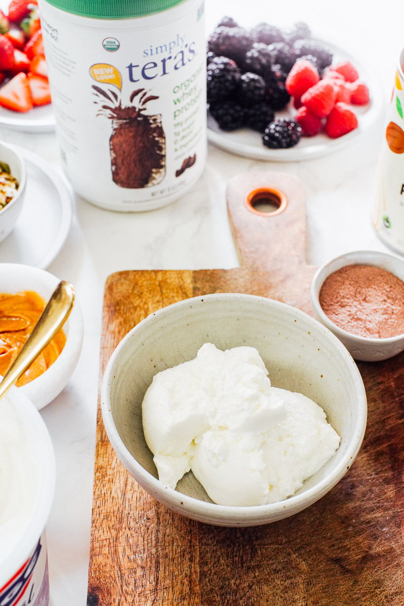 Yogurt in a bowl with chocolate protein powder in the background.