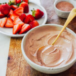 Chocolate yogurt in a bowl with strawberries in the background.