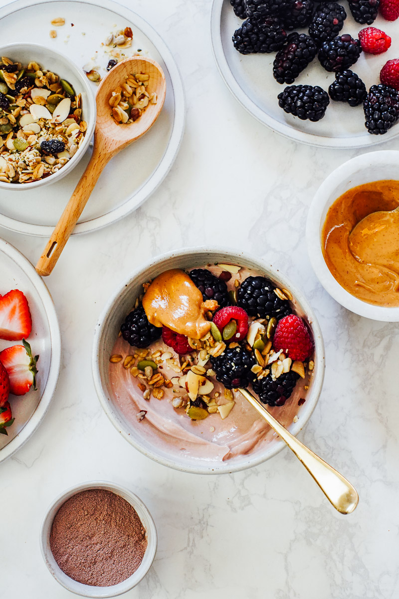 Adding toppings to the yogurt bowl: peanut butter, berries, and granola.