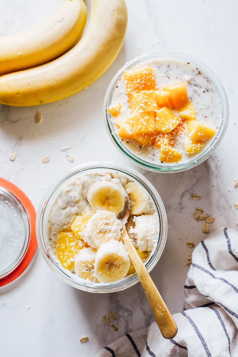 Overnight oats in glass jars topped with mango, pineapple, and banana.