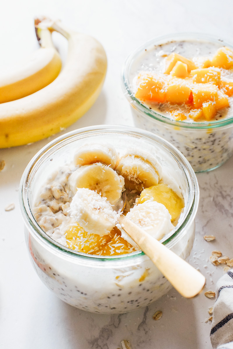 Overnight oats in glass jars topped with mango, pineapple, and banana.