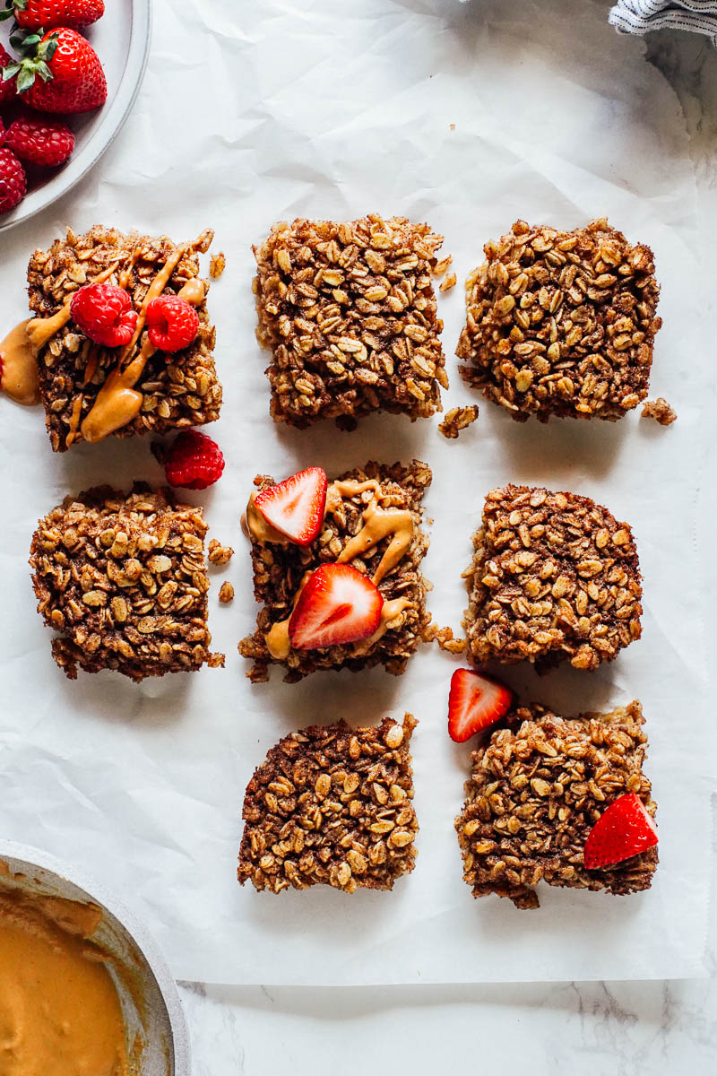 Oatmeal bars on parchment paper with strawberries and peanut butter on top.