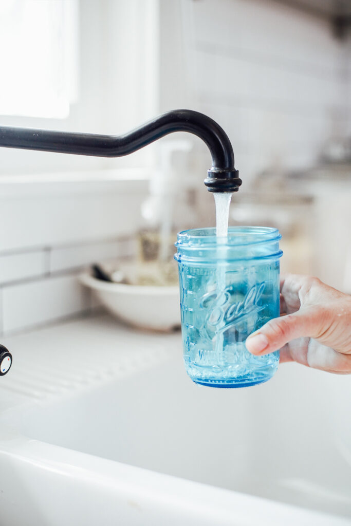 Adding water to a mason jar from the sink. 