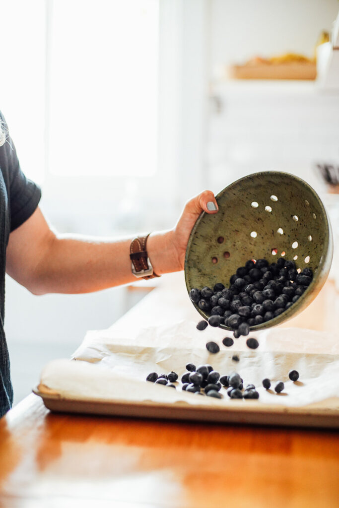 Pouring washed and dried blueberries from a colander onto a sheet pan. 
