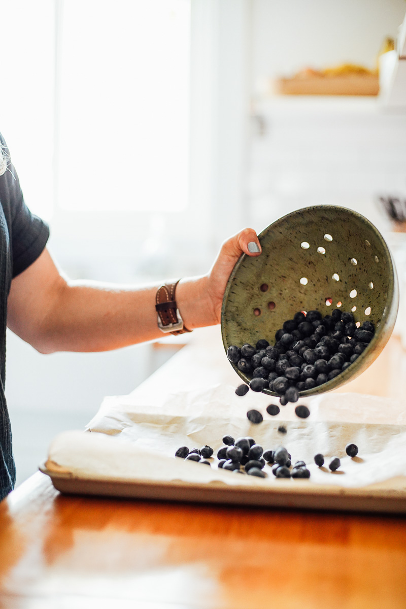 Pouring berries from a colander onto a sheet pan to freeze.