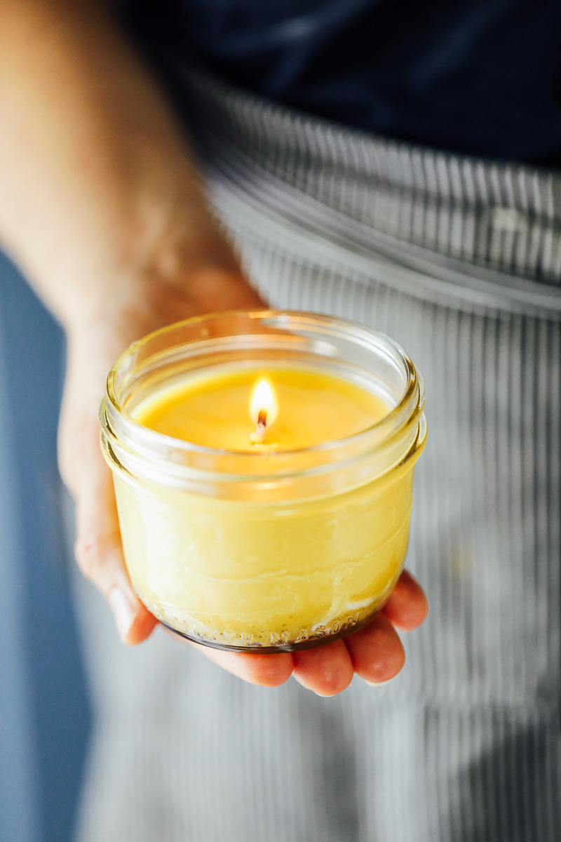 Holding a beeswax candles, lit with a flame. 