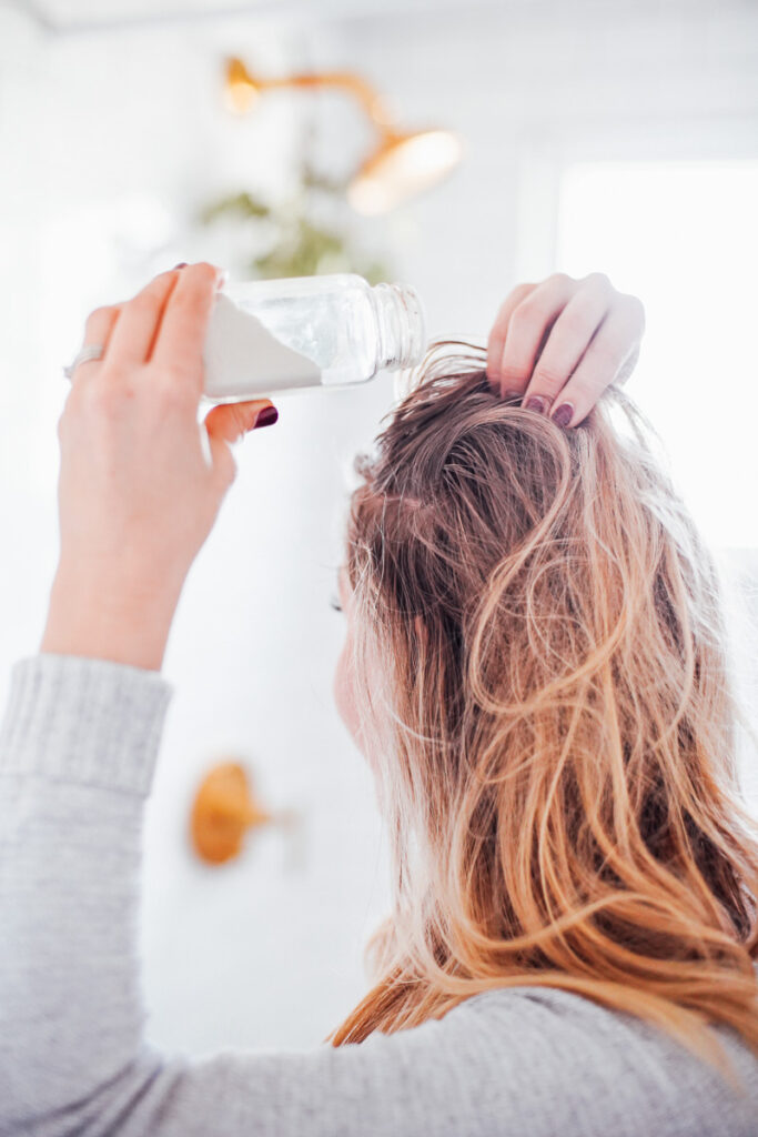 Sprinkling dry shampoo in hair, near roots.