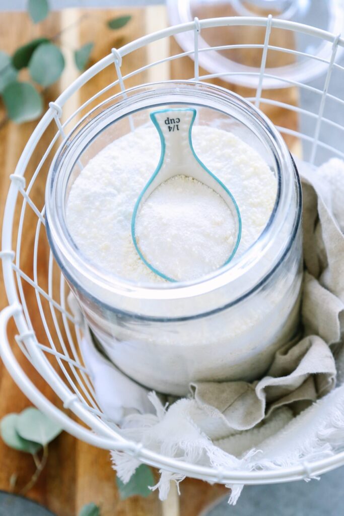 Laundry soap powder in a clear glass container with a scoop.